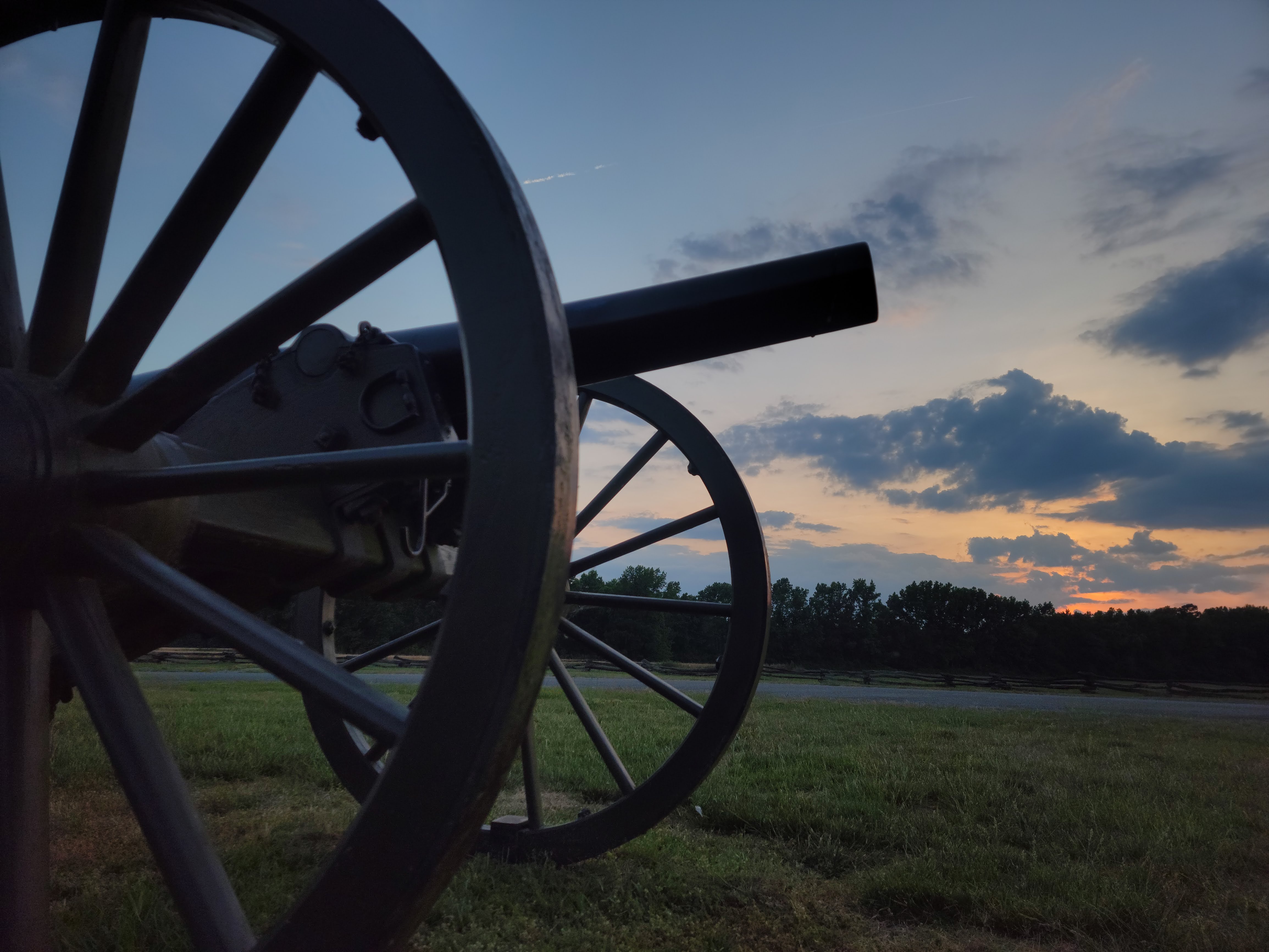 Bentonville Battlefield State Historic Site at sunrise. Morning light peaks through clouds over field viewed from ground level, closeup of cannon in foreground and overhead.