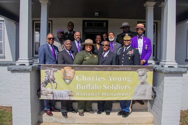 Group of people on a porch holding a banner reading "Charles Young Buffalo Soldiers Na