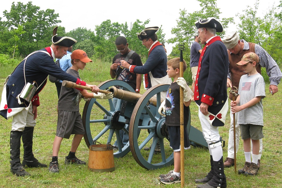 Revolutionary War living historians demonstrating to youth how to fire a cannon