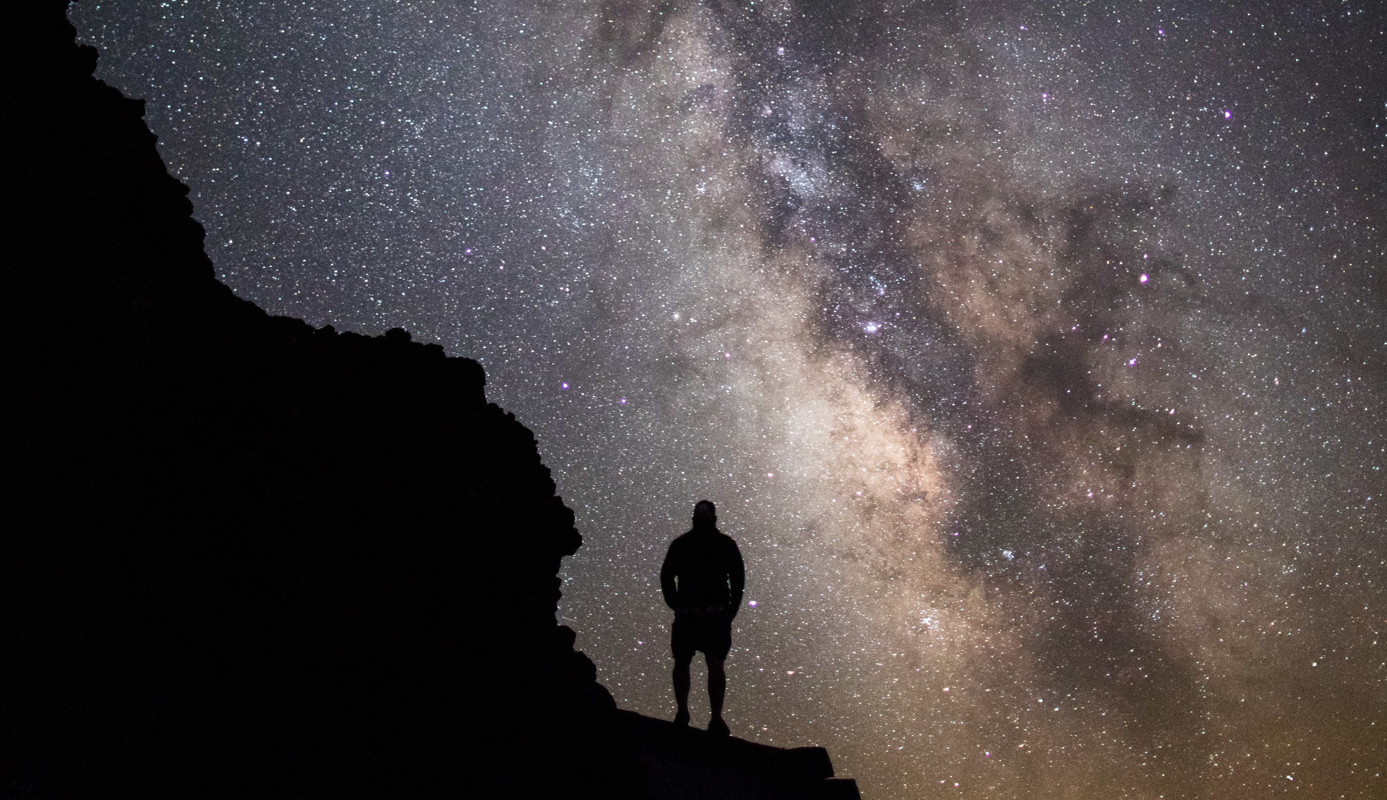 Silhouette of a person standing on an overlook at night looking at the Milky Way and a dark sky filled with stars. Silhouette of a person standing on an overlook at night looking at the Milky Way and a dark sky filled with stars.