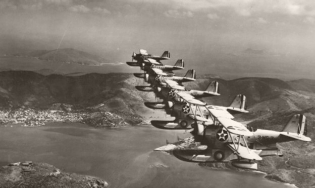 A black and white photo of military planes flying over the ocean