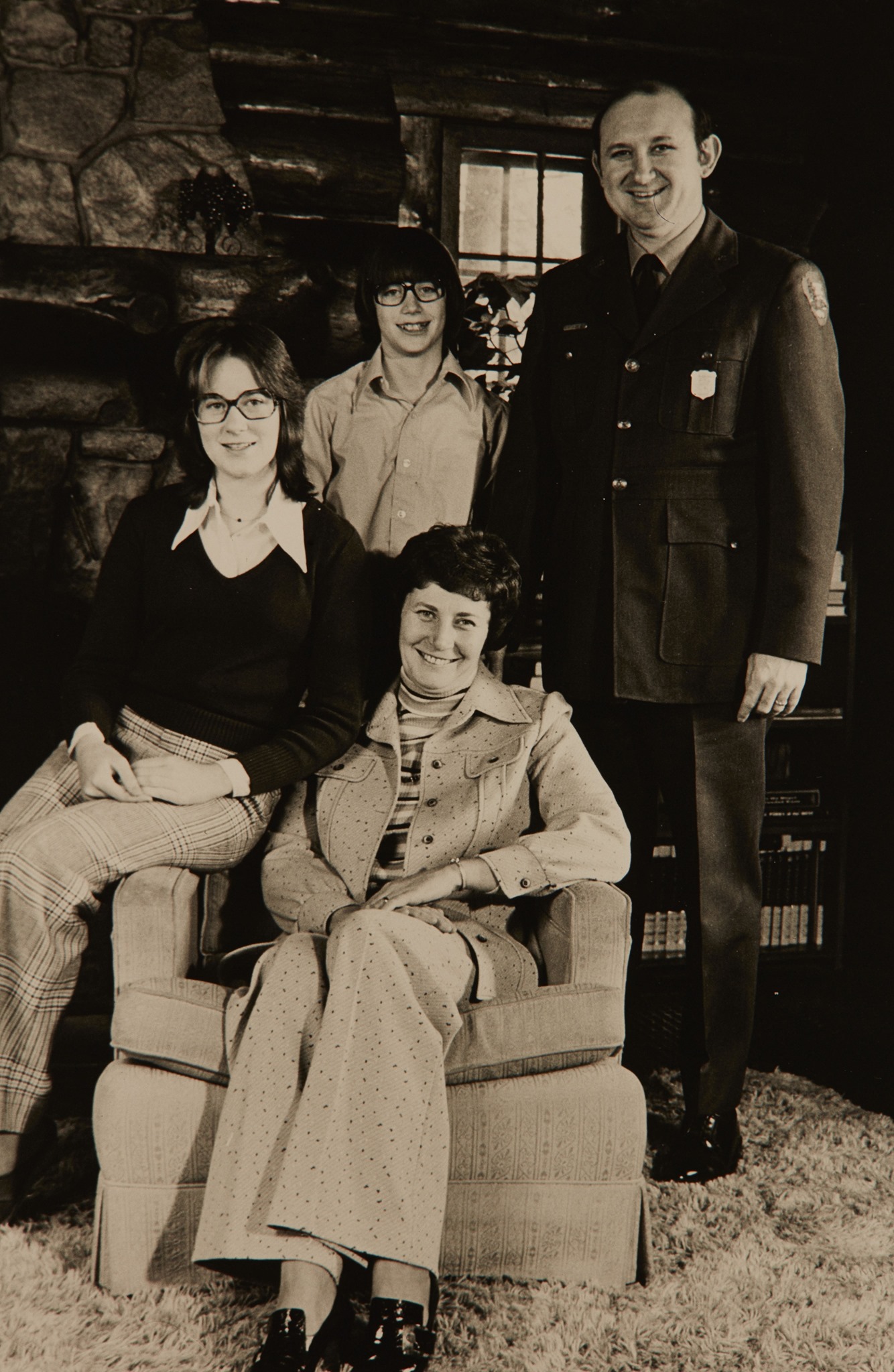 A sepia-toned family portrait. A man in a NPS uniform stands next to a son with glasses. A woman sits on an armchair in front, with a daughter with glasses on one arm of the chair. All are smiling.