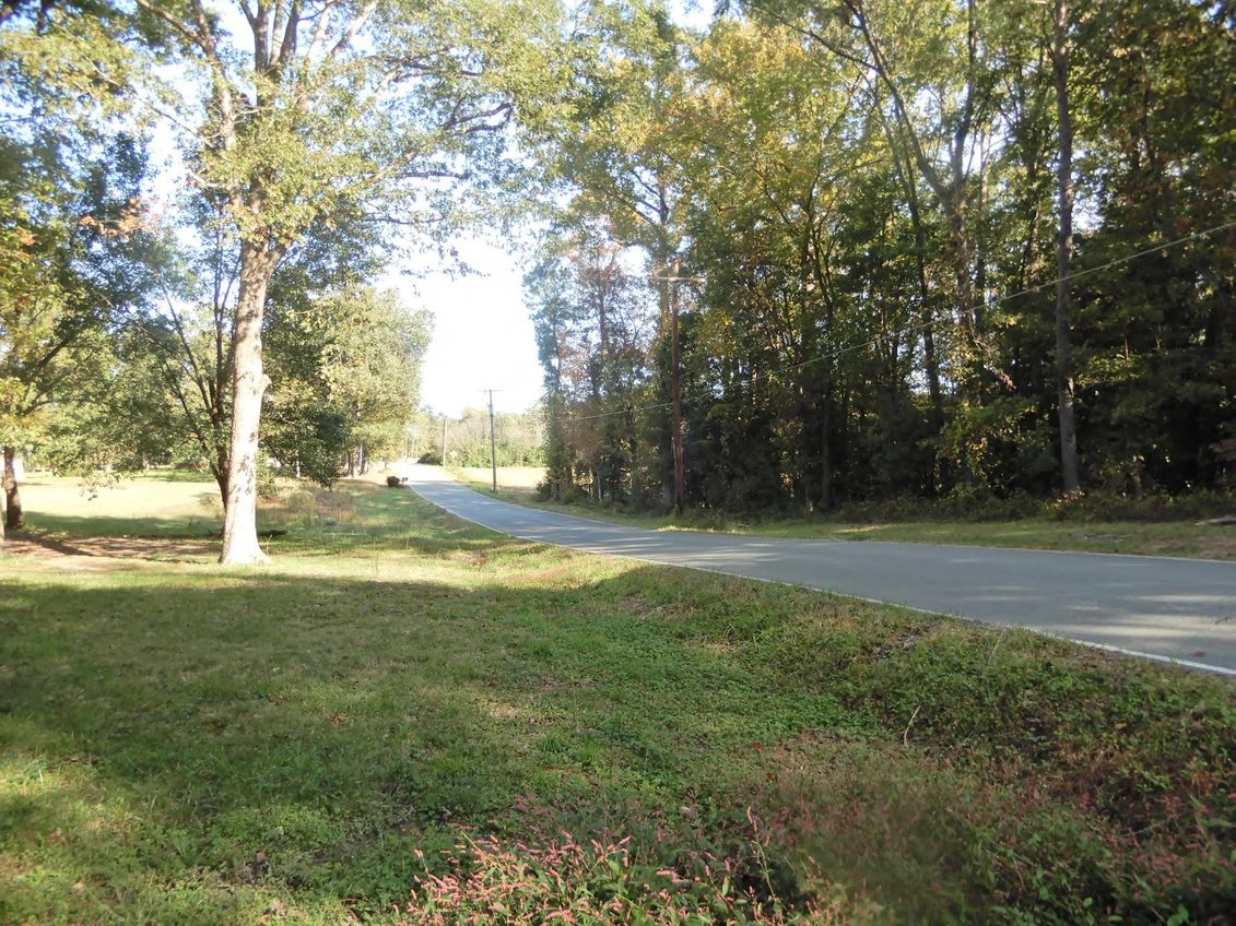 Fussell's Mill A two-lane blacktop highway stretches into the distance from right to center. On the left are trees and grass; on the right are trees and power lines.