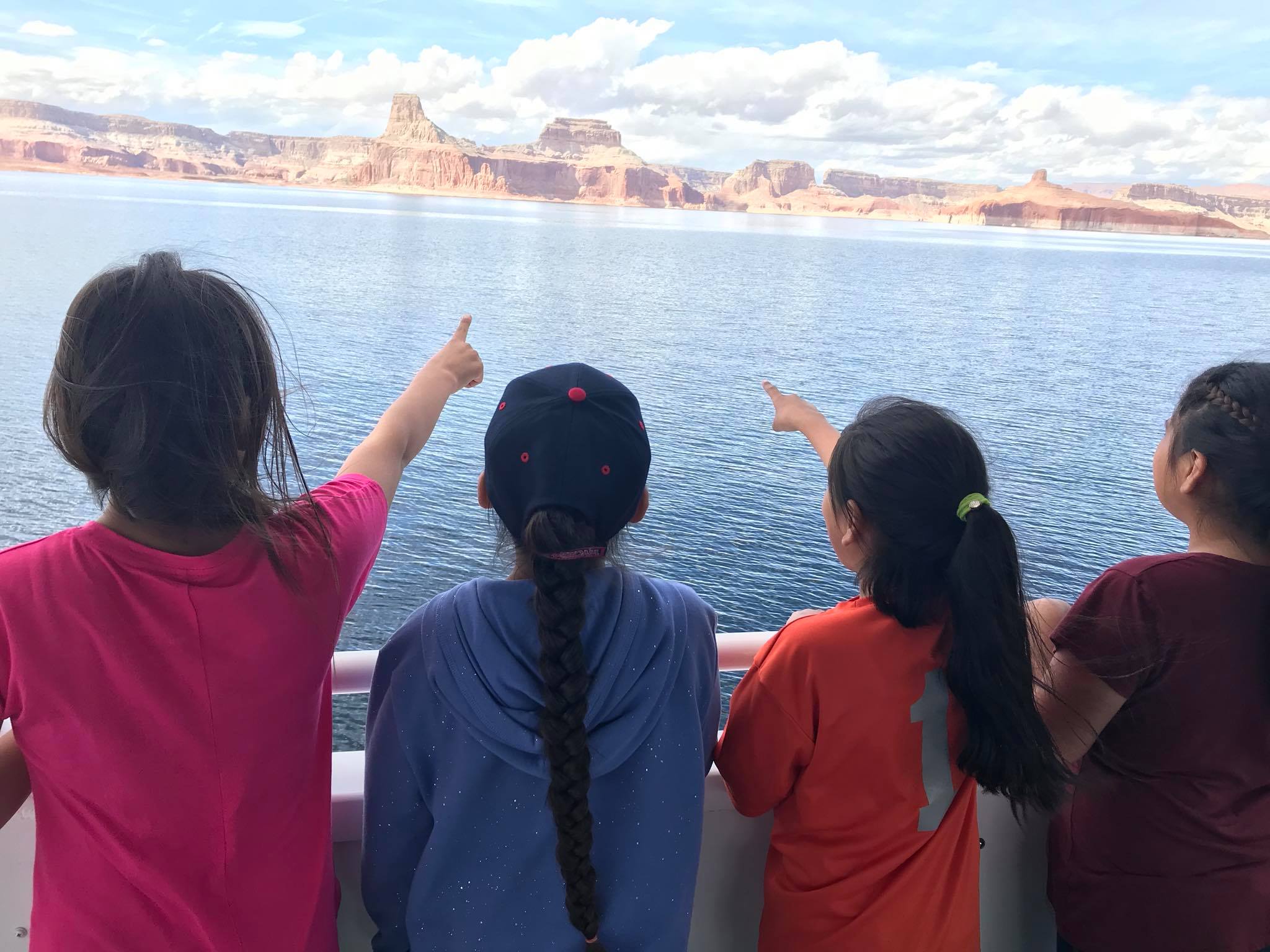four kids on a boat pointing across the water to a canyon wall