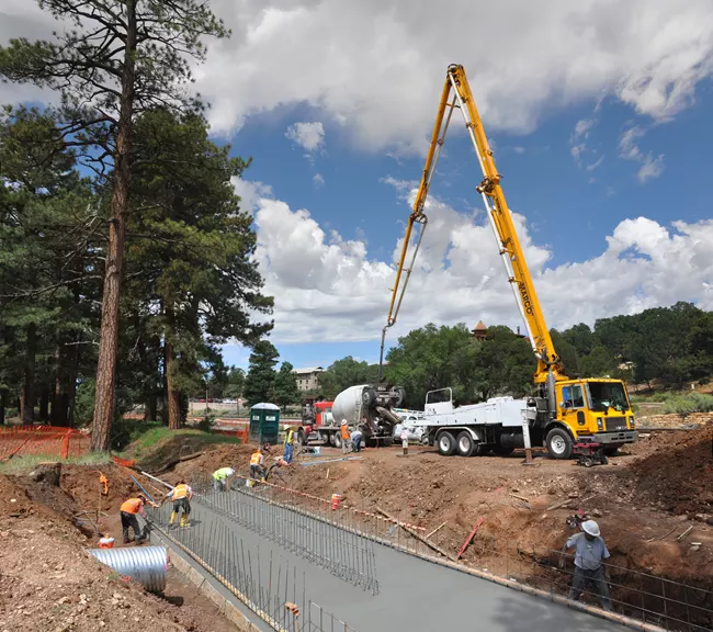 Large construction crane above concrete being poured for new sidewalk.