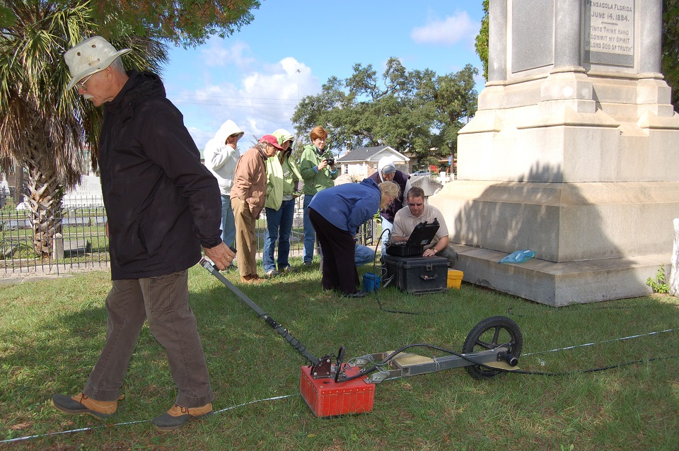 Man pulling a ground penetrating radar near a monument while other view the results on a computer