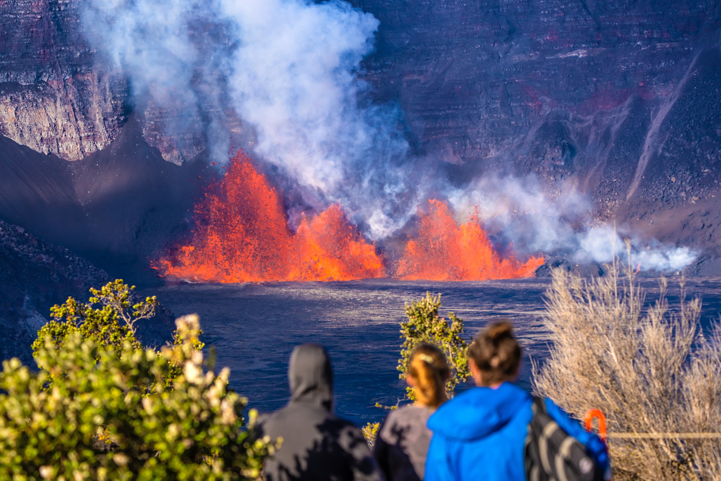 People stand looking onward to an eruption of bright orange lava