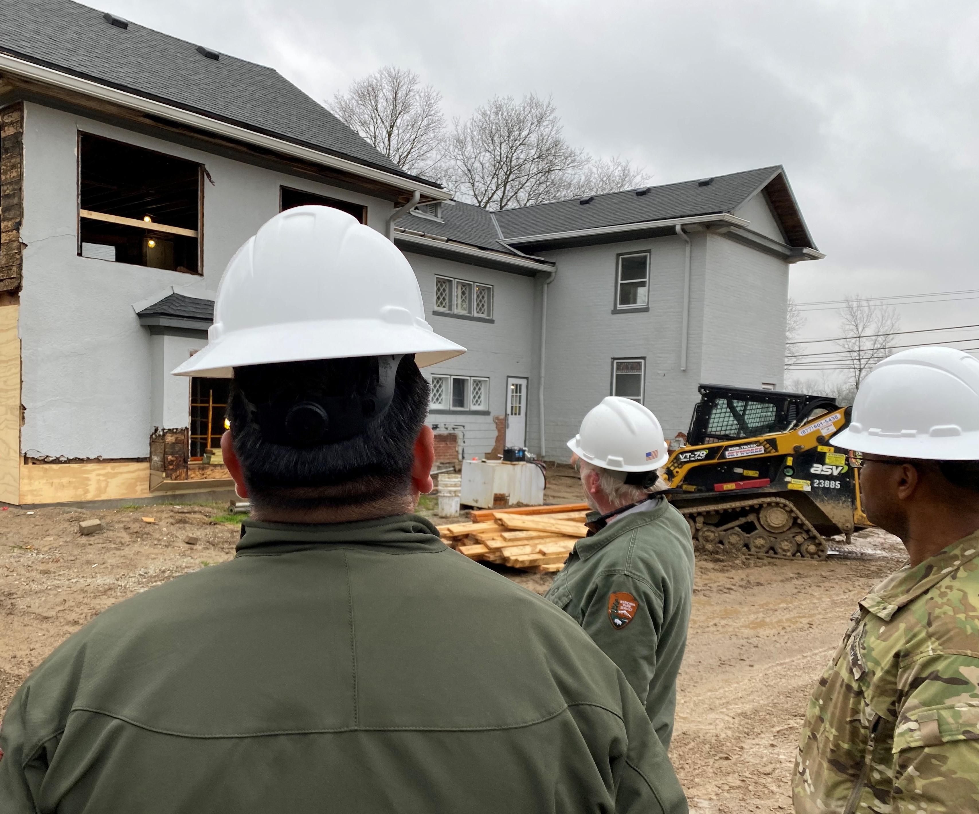 Three people in hard hats look at construction work taking place on exterior of historic home.