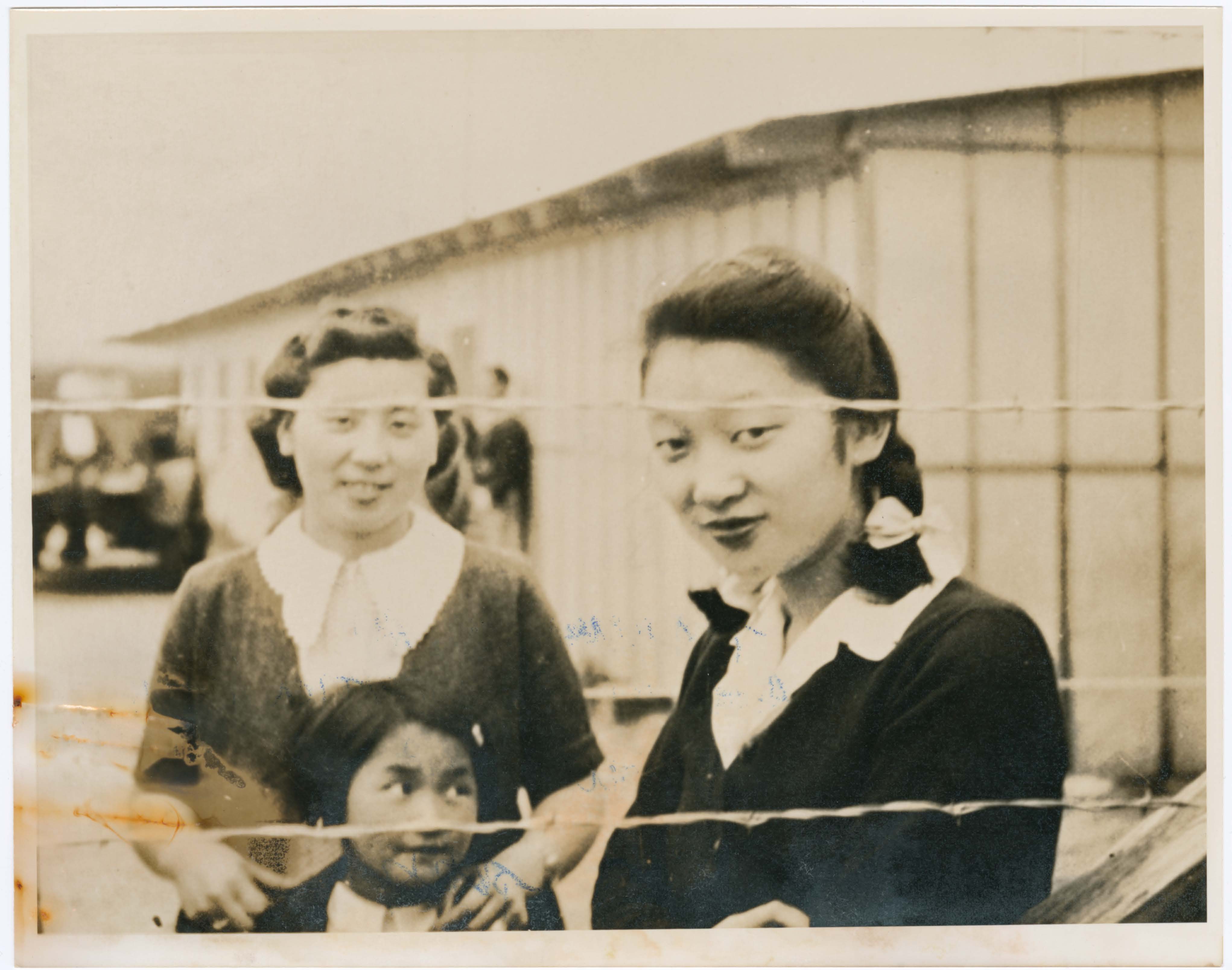 Two women and a young child behind a chain link fence.