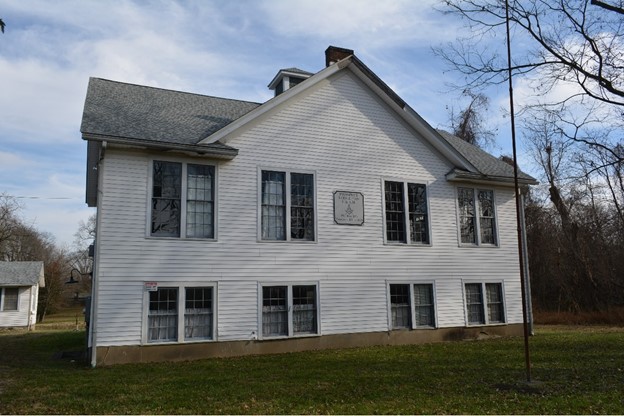 The Jefferson Jacobs Rosenwald School, a white, two-story schoolhouse, on a grassy lot with trees in the foreground located in the Taylor-Jacob Subdivision in Louisville, Kentucky.