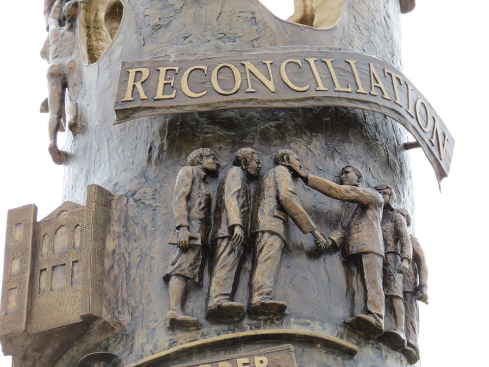 JohnHopeFranklinReconciliationPark_ReconciliationTower Close up of the dark bronze Reconciliation Tower. Two groups of men are depicted shaking hands below the word "Reconciliation".