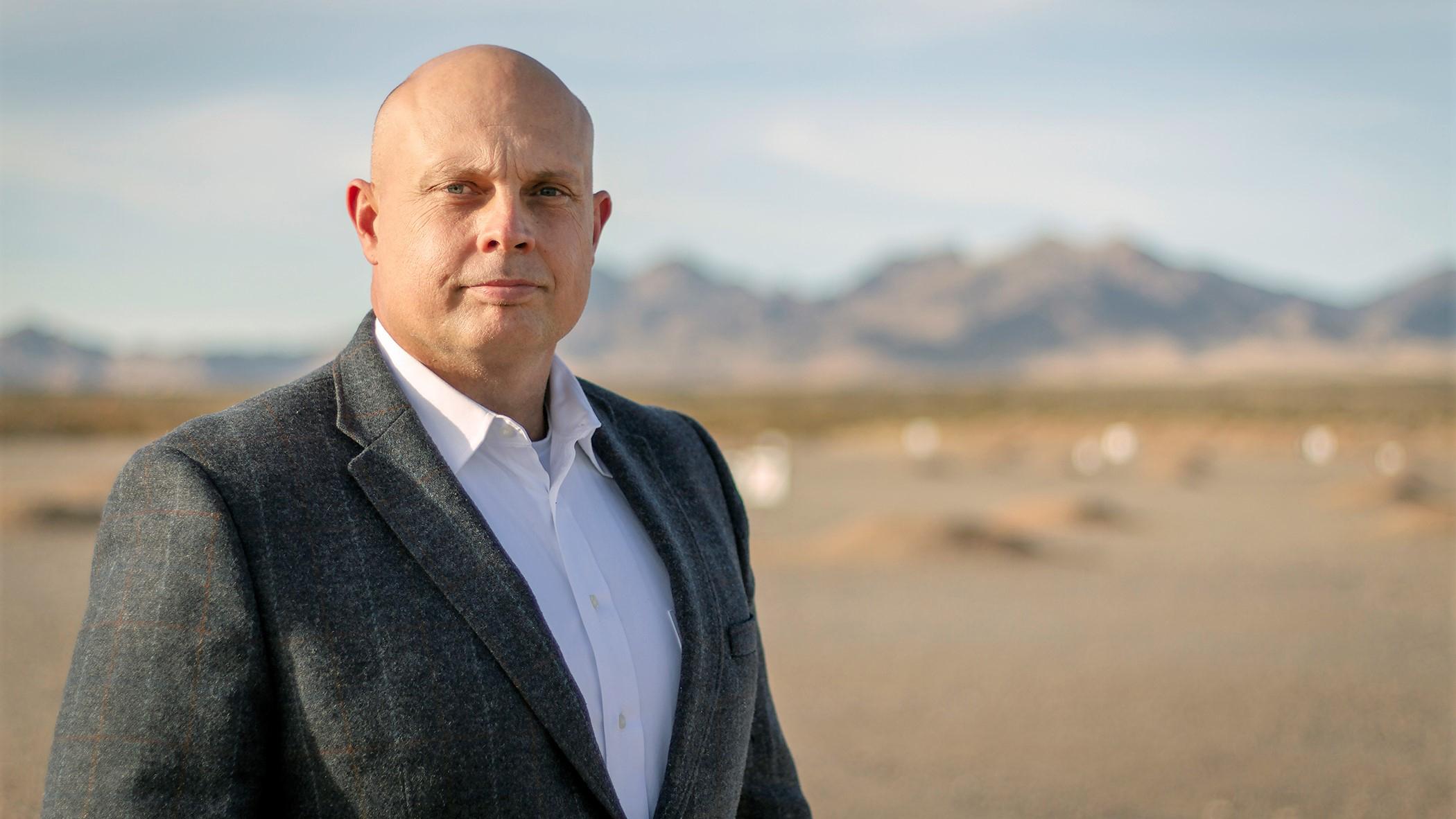 Man in a suit poses for a photo with a mountainous background