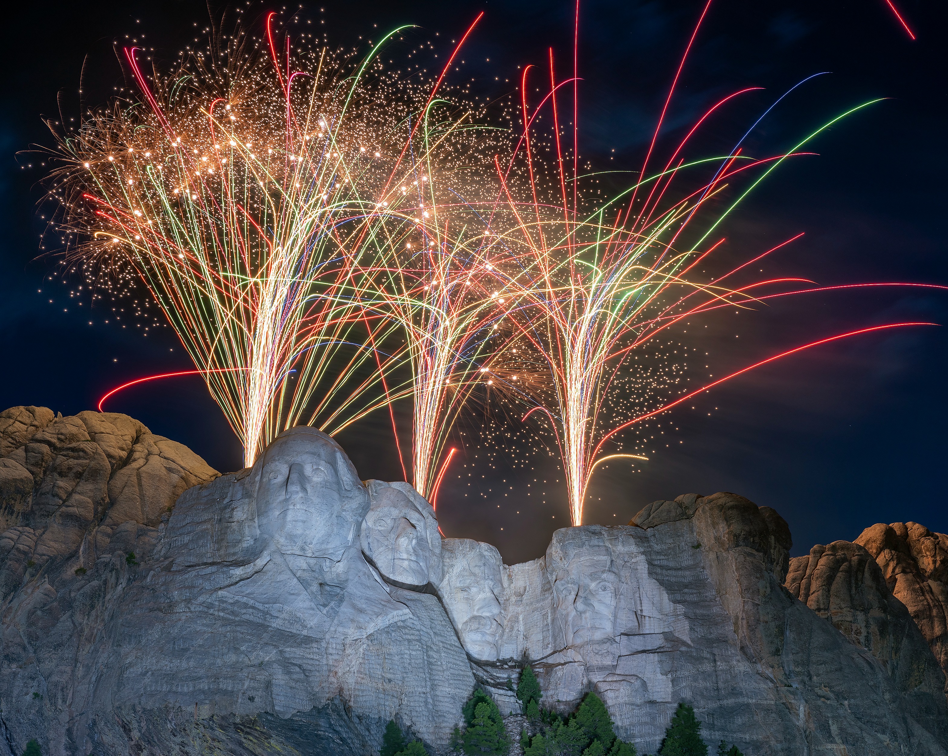 Multicolored fireworks in the night sky above the carvings of the presidents on Mount Rushmore.