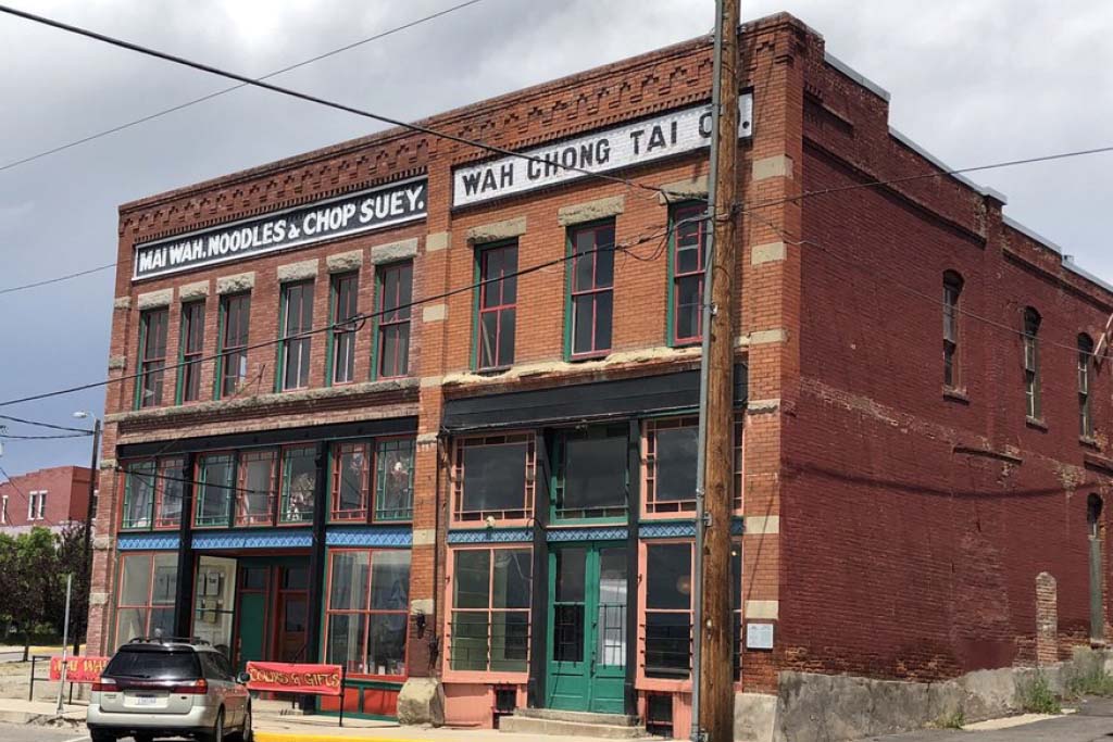 Brick building with store front painted on top reading Mai Wah Noodle Parlor and Wah Chong Tai Company