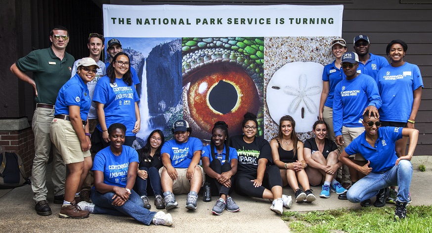 Group of youth standing or sitting by a Centennial banner