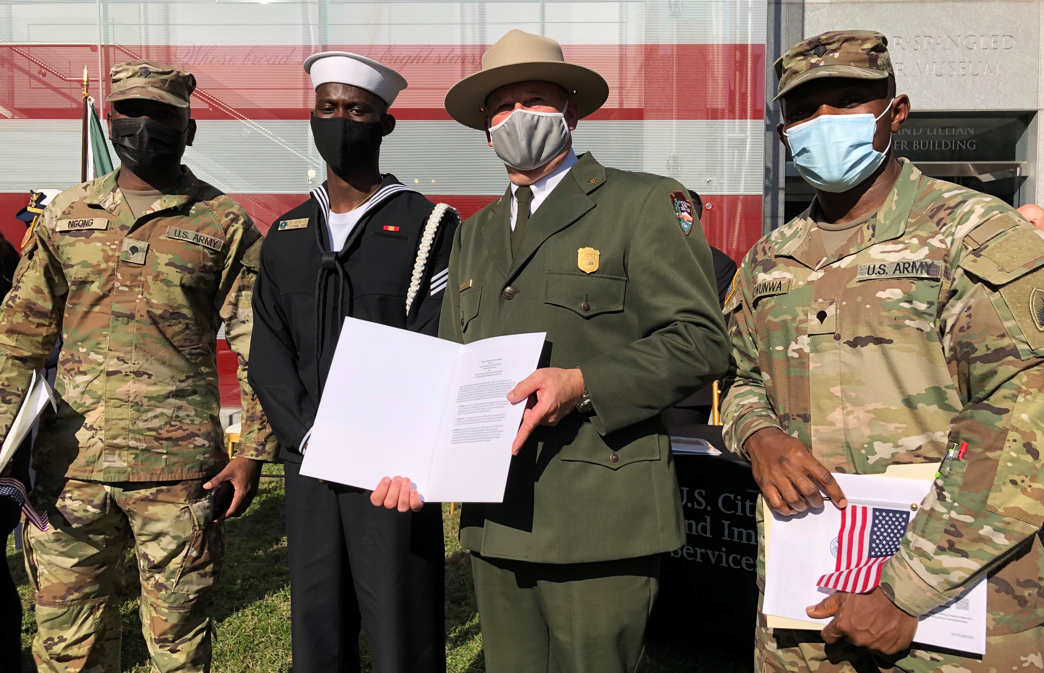 Three members of the U.S. Armed Forces stand with NPS Deputy Director at a naturalization ceremony. Two U.S. Army soldiers in camouflage fatigues and one U.S. Navy sailor stand with park ranger who is holding a document.