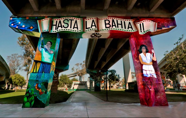 A mural painted on the supports of an underpass in a grassy park.