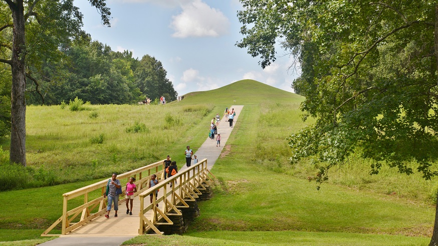 Families walking on a path down the side of a prehistoric earthen mound