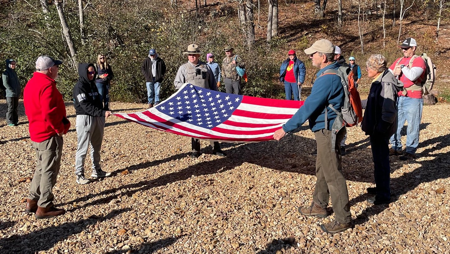 Park ranger and military veterans hold open the US flag on a park trail