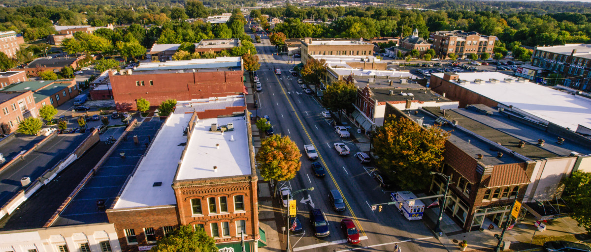 A view of a city intersection with low buildings and trees with yellow, orange, and green leaves dotted throughout.