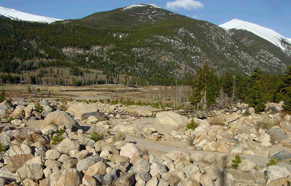 Trail through a rocky valley with a forested mountain in the background