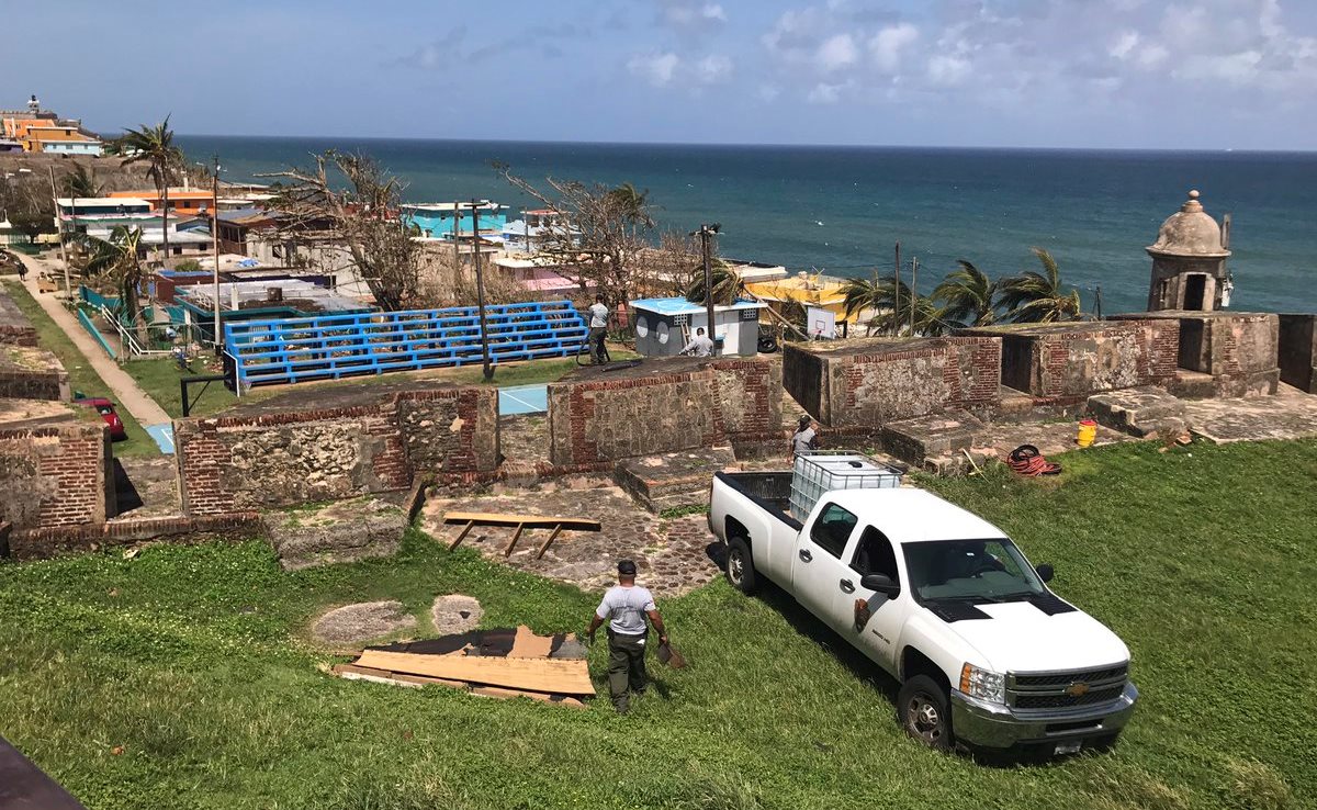 San Juan NHS staff providing non-potable water to neighbors of La Perla after Maria NPS pick up with tank in the truck bed and an employee near fort wall with private homes on the other side of the wall