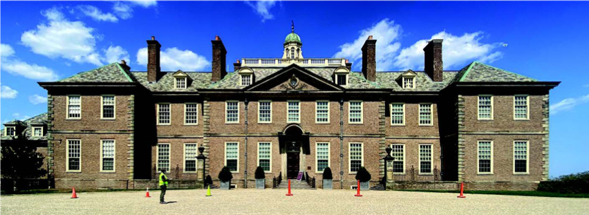 A wide two-story brick building with a cupola, four chimneys and four dormered windows.