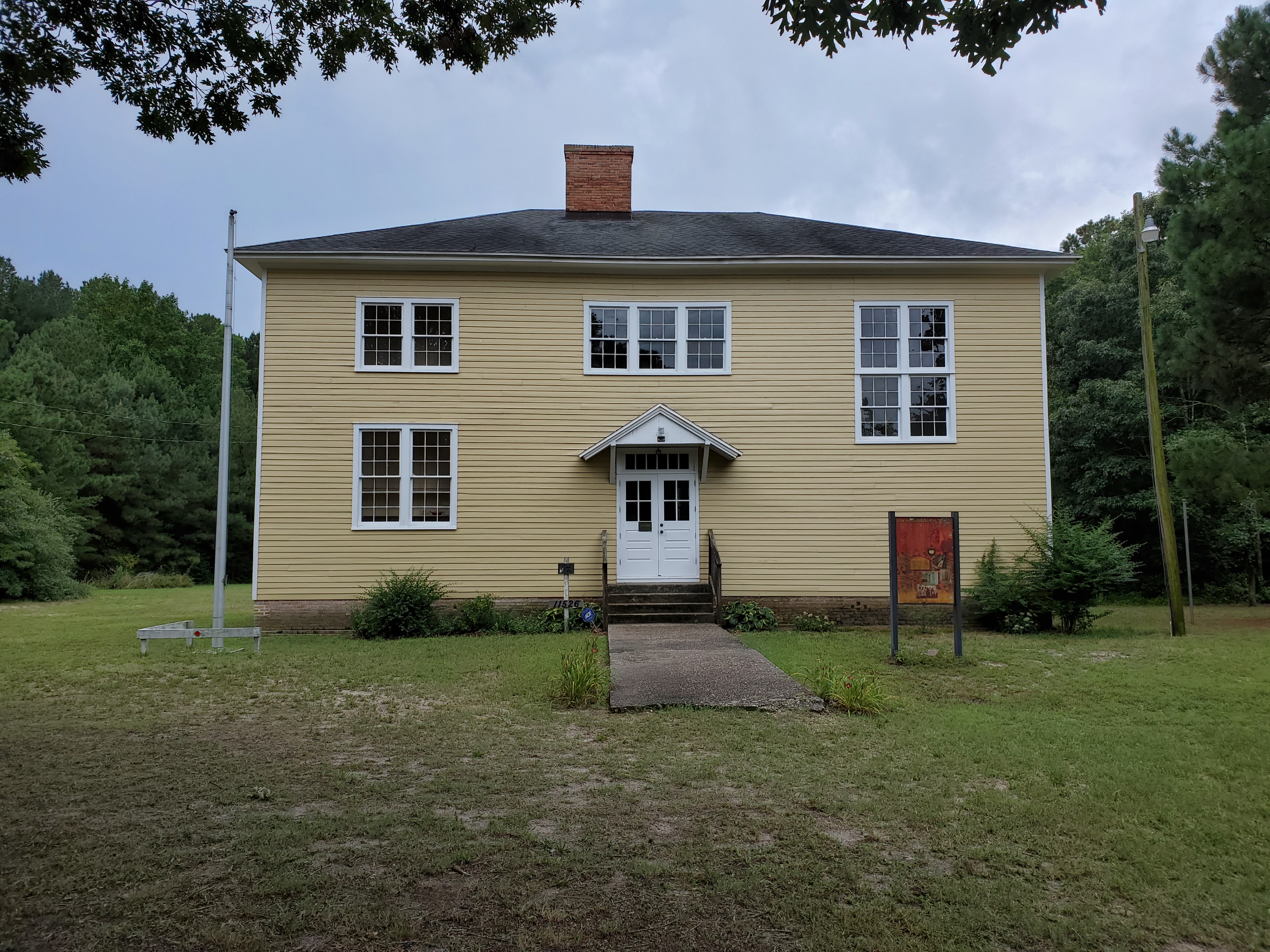 San Domingo School Two-story yellow building with a chimney and white-trimmed door and windows.
