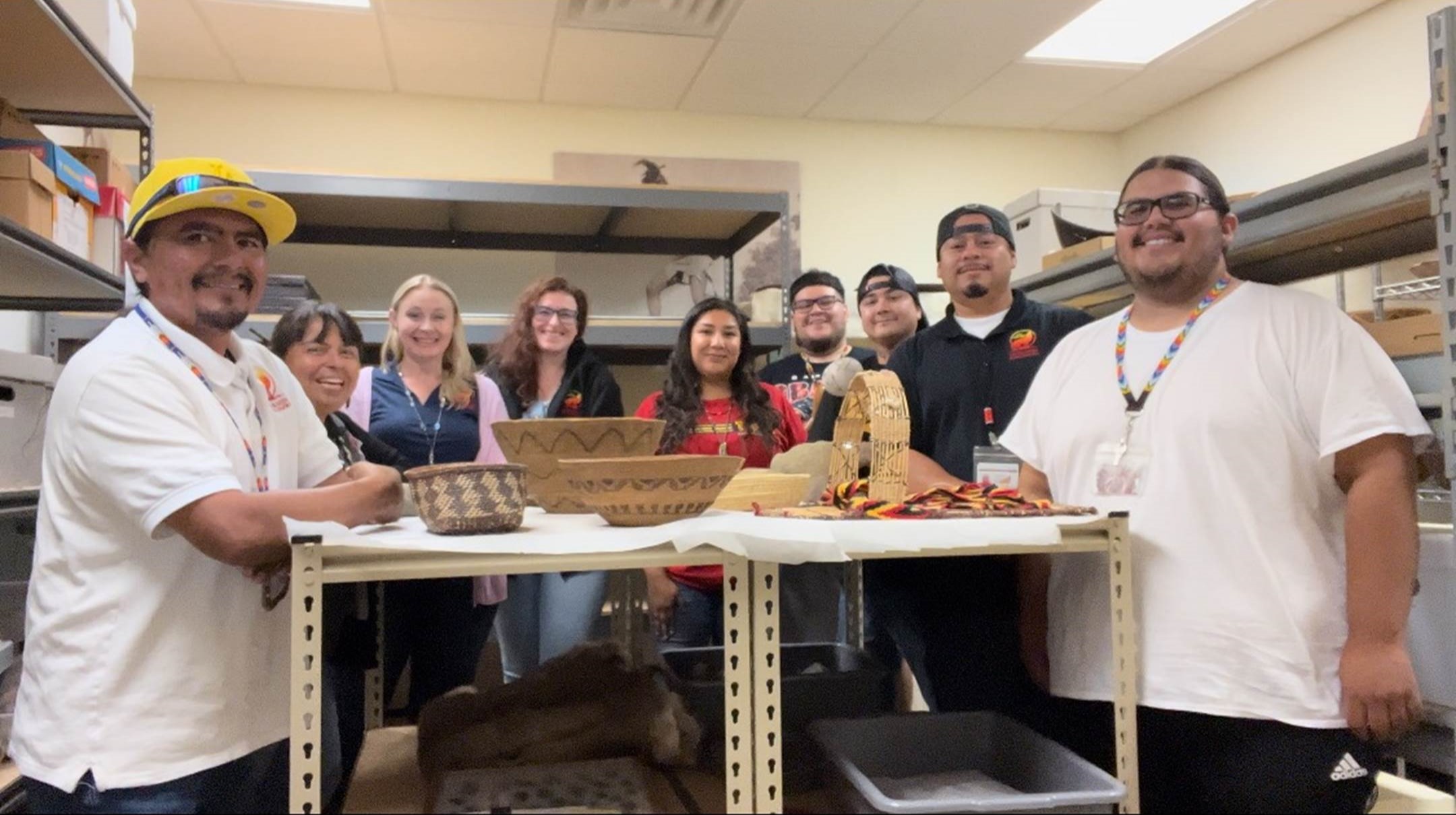 Nine people stand around a table with Tribal artifacts on the table.