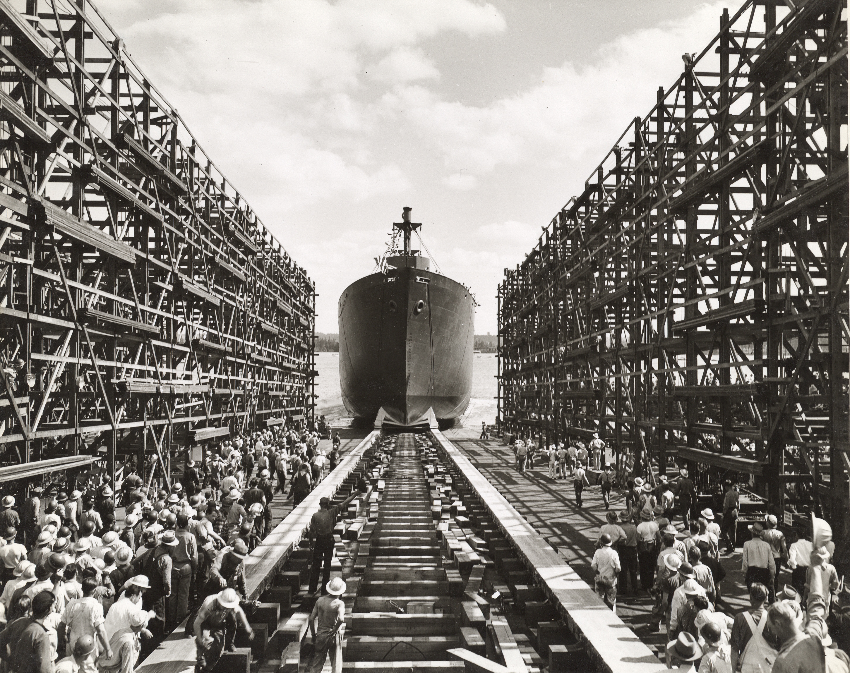 Ship launching from dry dock as workers look on