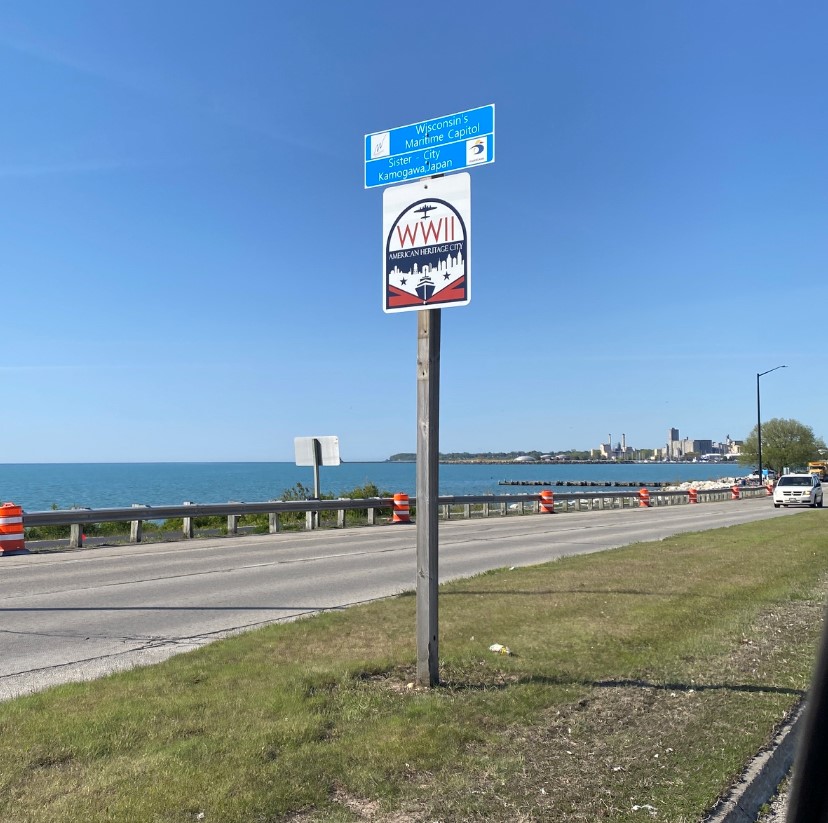 American World War II Heritage City Program in Wisconsin A street sign displays two signs and a city is shown in the background.