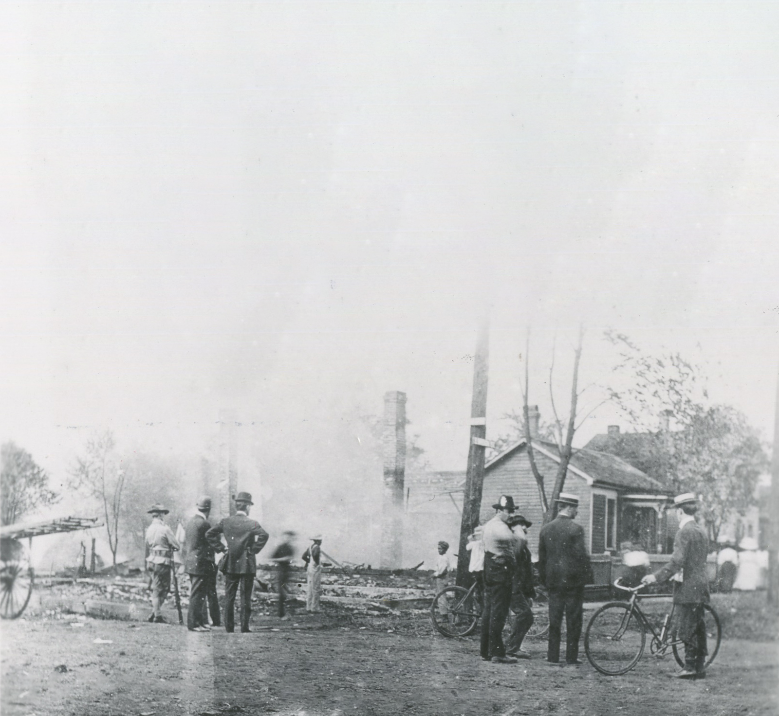 Facing away, men look at the remains of a burned building.