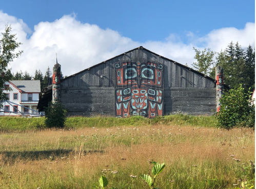 A large and grey wooden house with Tribal art painted on the outside in a grassy field.