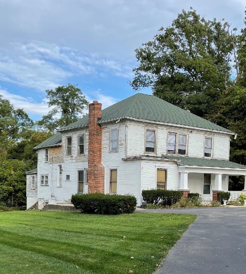 Two story historic home with dilapidated siding and a brick chimney