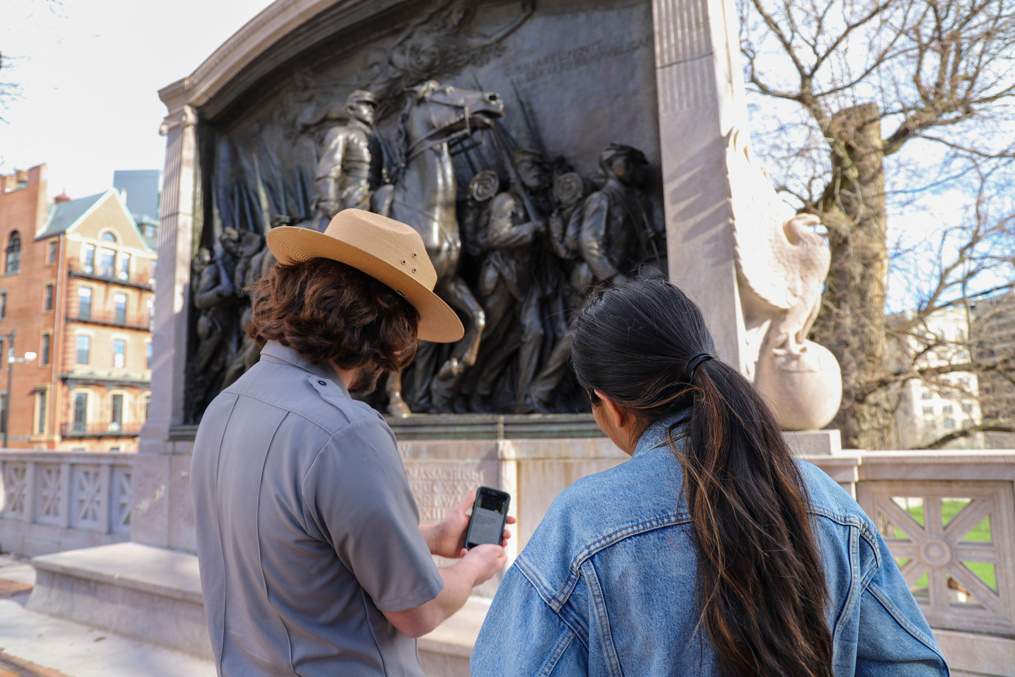 Ranger showing a visitor the Travel with Tubman tour on their phone. A park ranger points at the NPS App on a visitor's cell phone while they stand in front of a monument dedicated to African American soldiers