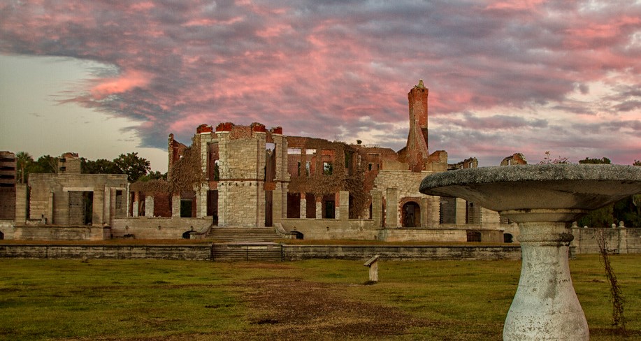 Photograph of a large plantation house in ruins on a cloudy day at sunset.