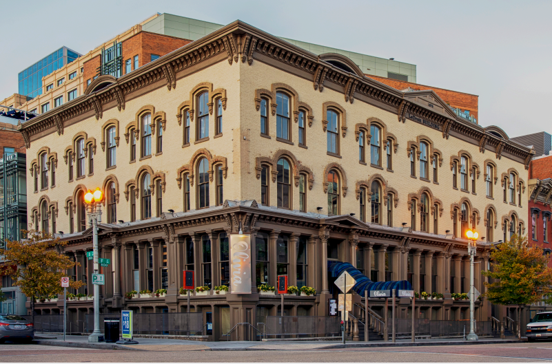 A three-story building on a city block lit by street lamps before dusk.