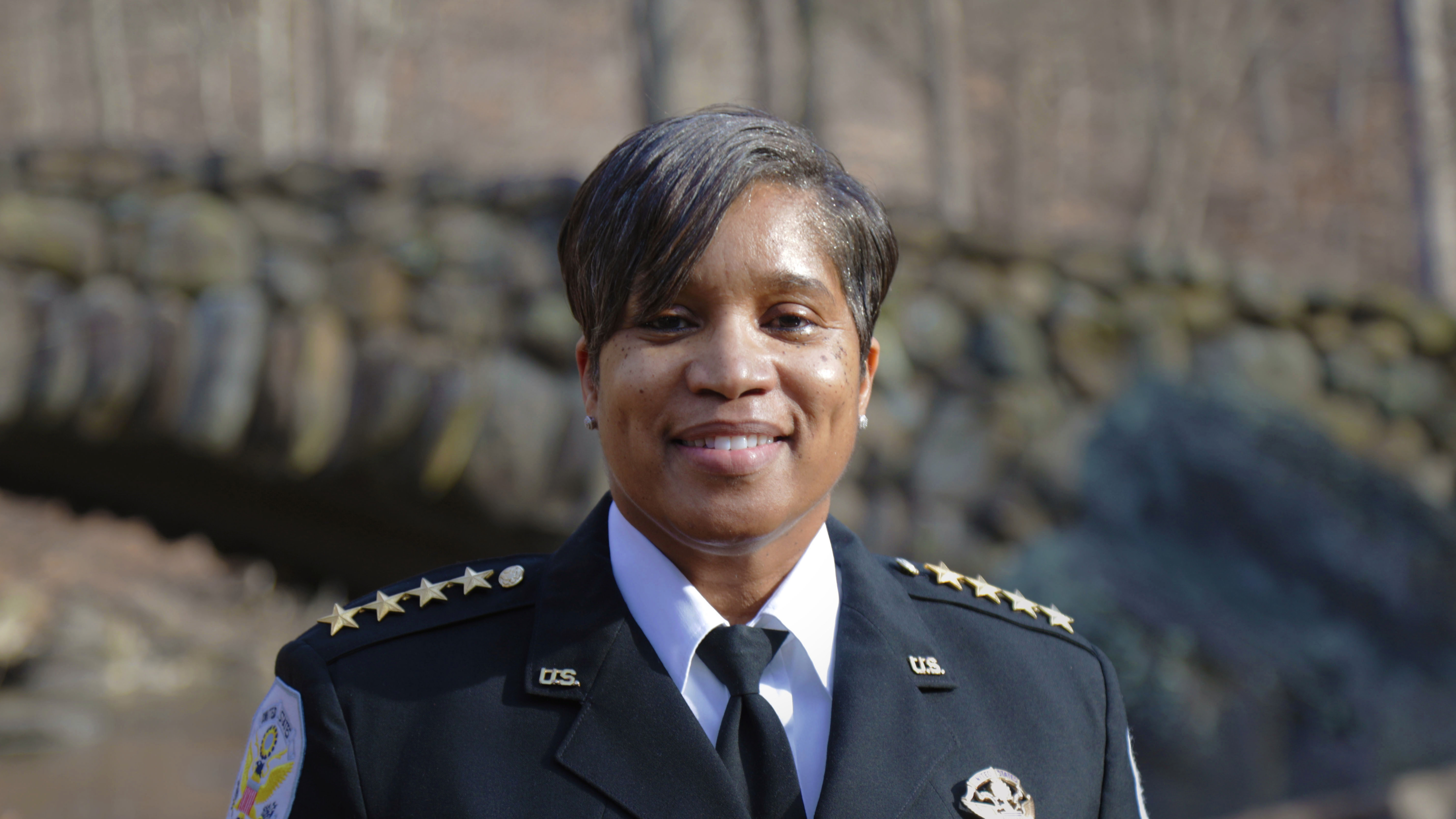Pamela A. Smith Chief of the U.S. Park Police stand in front of a stone bridge in Rock Creek Park.