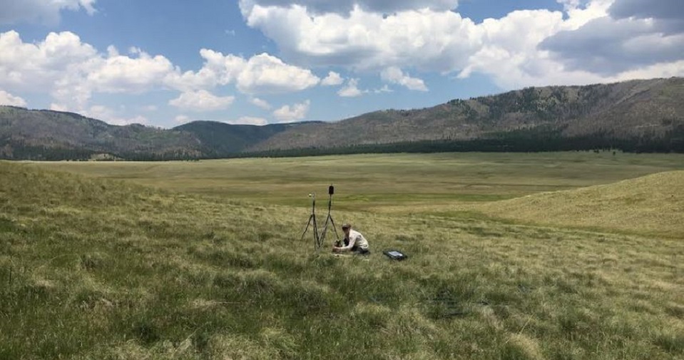 Scientist setting up a tripod and sound equipment in a grass field