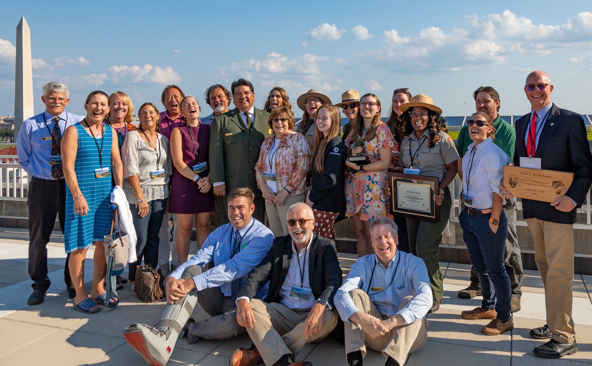 A large group of people stand together, some holding awards, with NPS Director. The Washington Monument is off to the side.