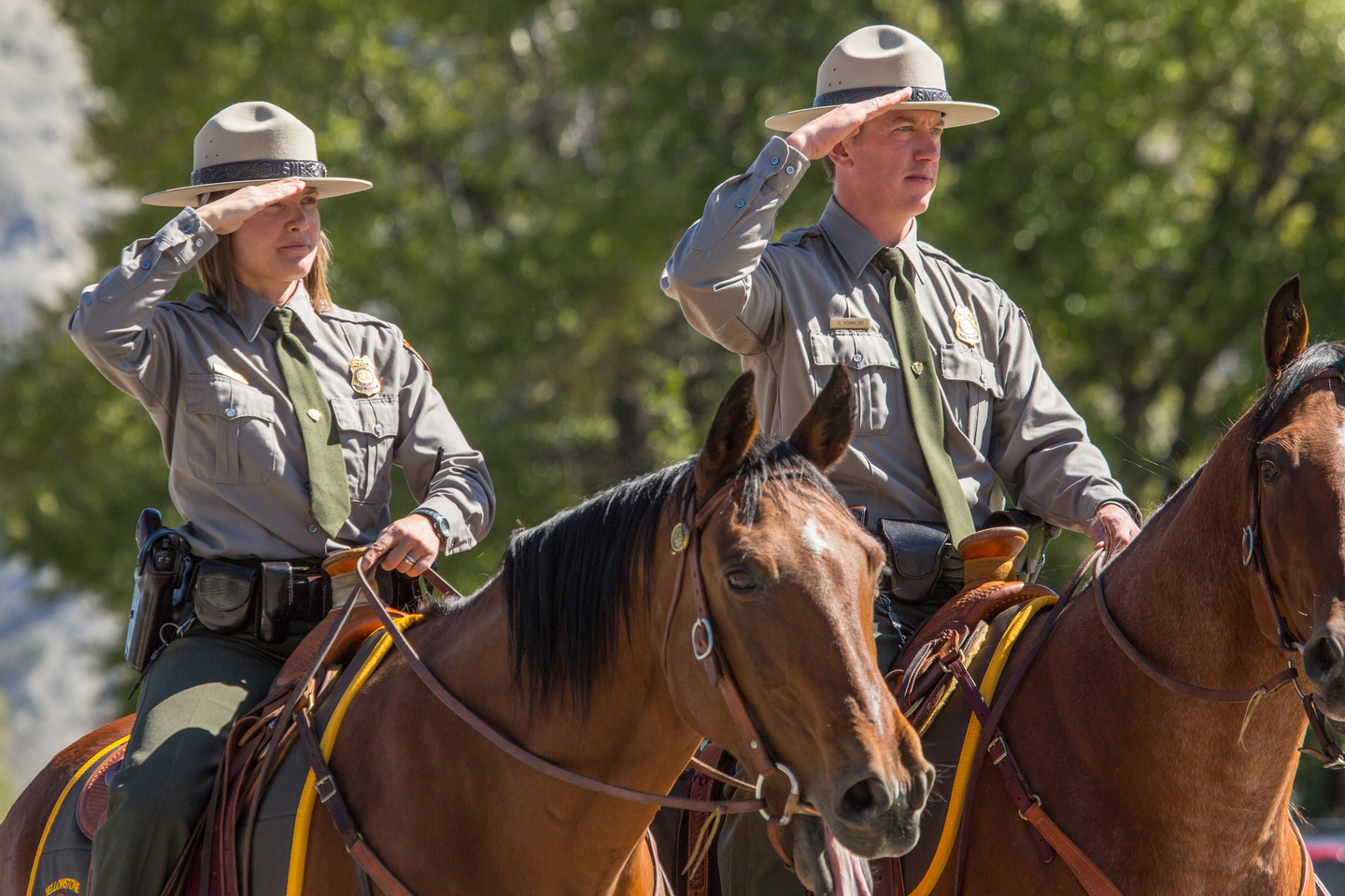 Two National Park Service law enforcement officers saluting while on horseback