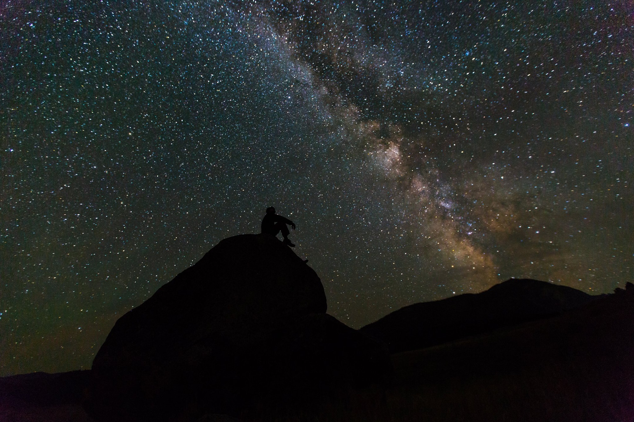 YELL visitor Silhouette of a person sitting on a boulder looking at the night sky filled with stars and clearly depicting the Milky Way.