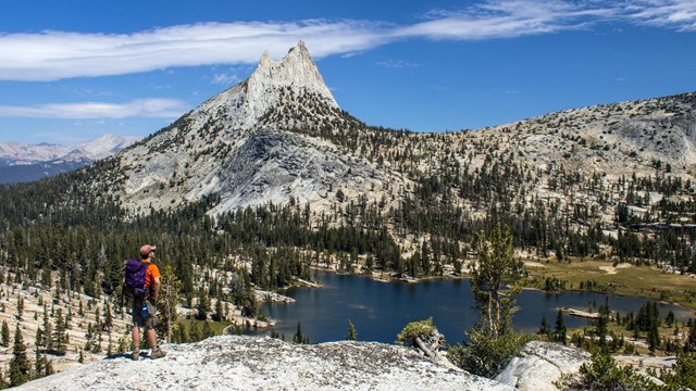 Visitor standing near a ledge overlooking a mountain, valley, and lake