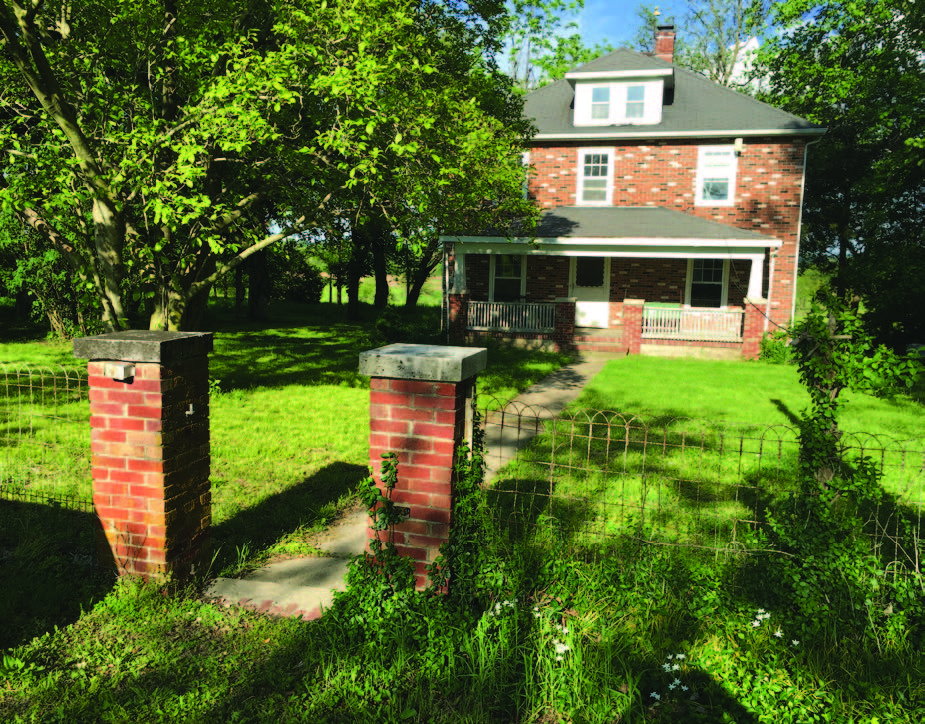 Old brick house with a chain fence and a tree in the front yard.