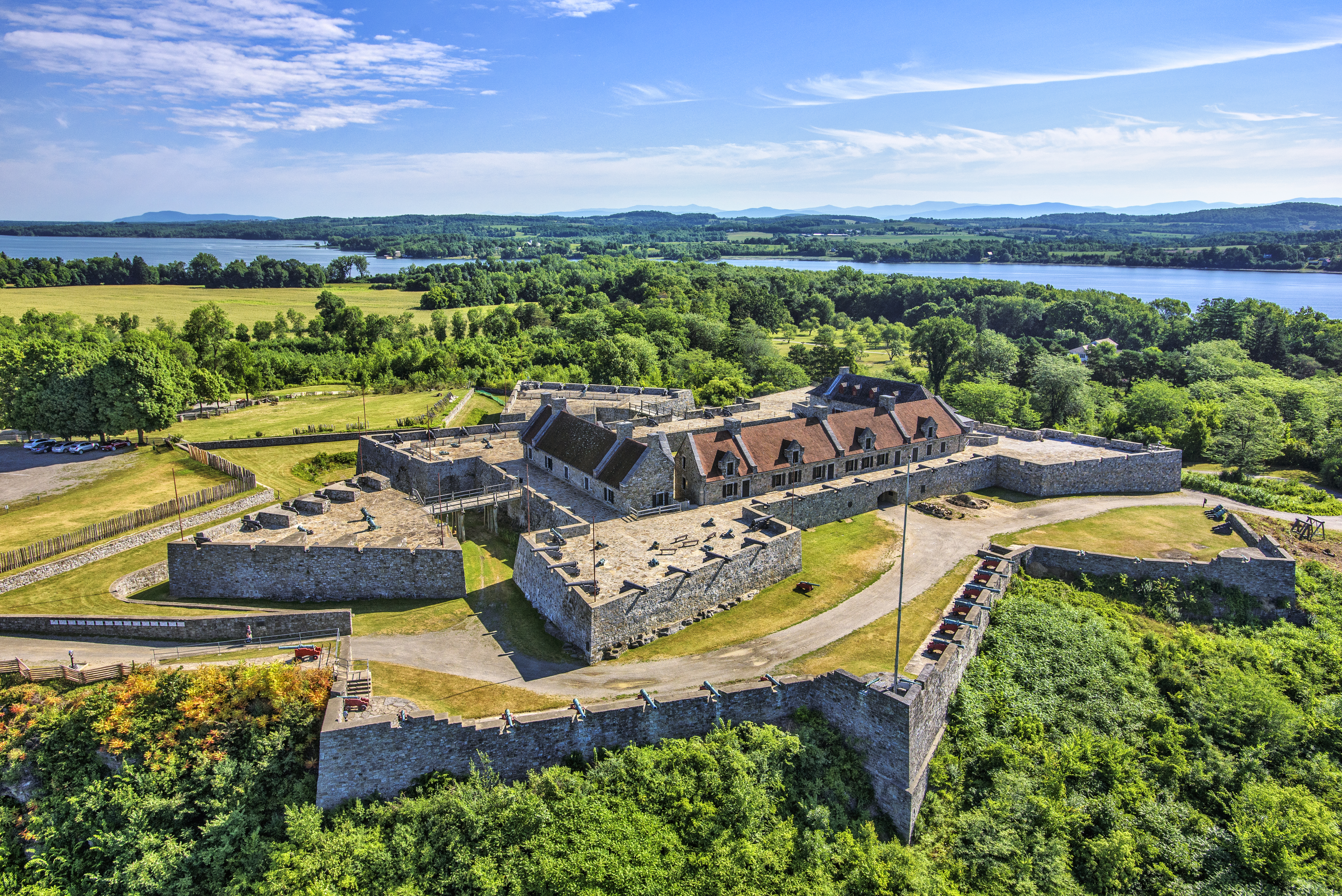 Star-shaped stone fort atop wooded hill, surrounded by lush forest and overlooking body of water.