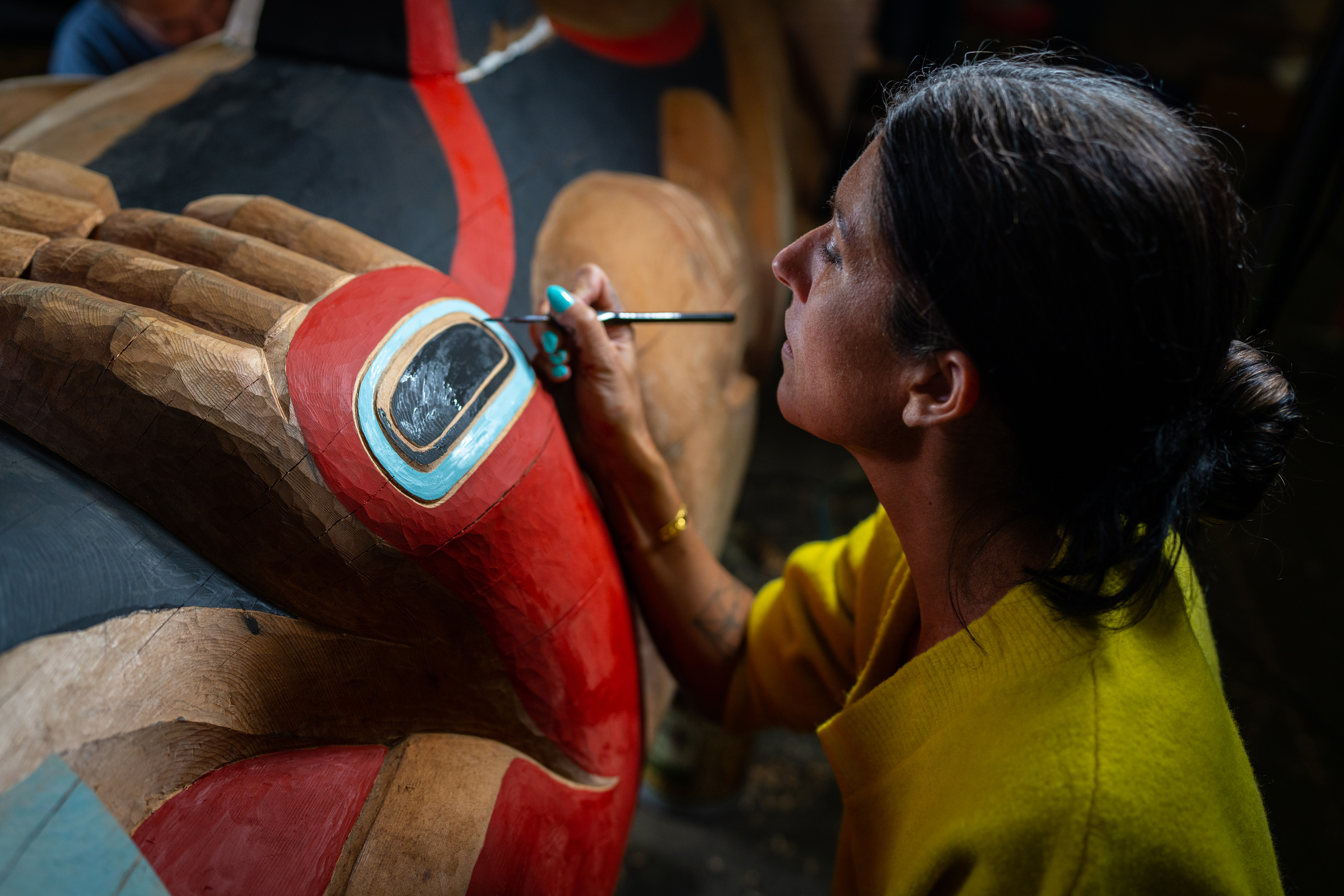 An artist paints a Kaagwaantaan totem pole multiple colors, including red, blue, and black. An artist paints a Kaagwaantaan totem pole multiple colors, including red, blue, and black.
