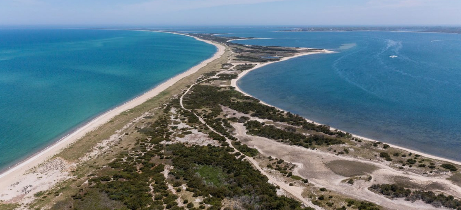 Nantucket Barrier Beach and Wildlife Refuge An aerial view of a narrow vegetated beach with blue water on either side of it. Triangular spits of land protrude into the water on the right side.