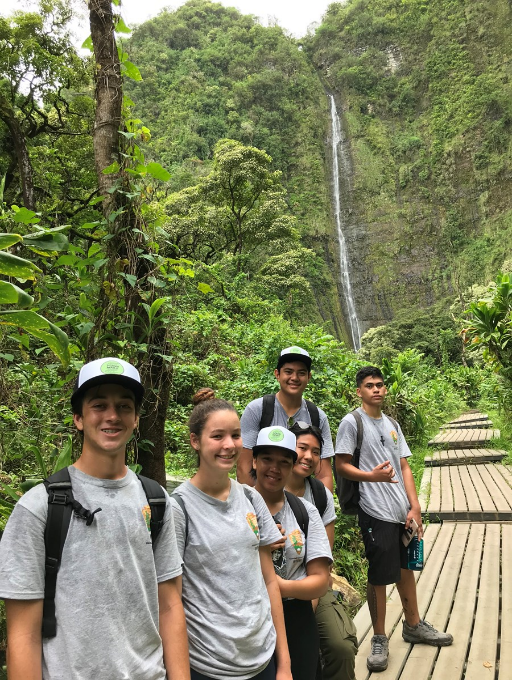 Six young people wearing matching t shirts and hats on a trail in a lush forest.
