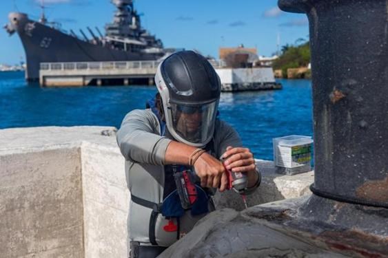 person wearing safety equipment using electric drill on concrete wall