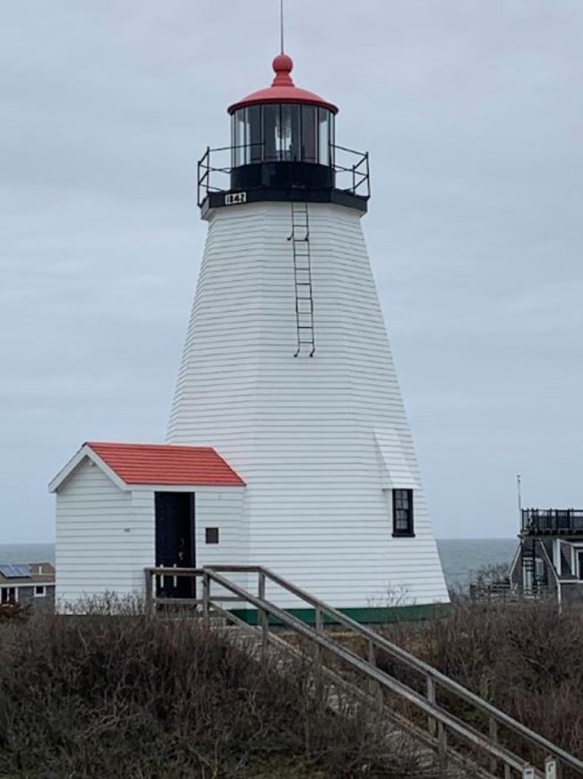 tall white lighthouse with small attached one room structure on bottom left side.